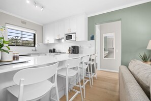Una cocina moderna con armarios blancos, una isla central con taburetes y electrodomésticos como microondas y cafetera.