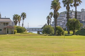 Ein Golfplatz mit einer Brücke, Palmen und Gebäuden im Hintergrund.