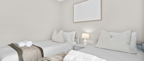 Habitación de hotel con dos camas, una mesita de noche con lámpara y una obra de arte en la pared.