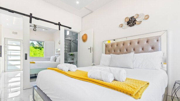 A modern bedroom with a large bed, a sliding door leading to a balcony, and a decorative wall piece.