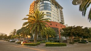 Ein mehrstöckiges Hotel mit geschwungener Fassade, Palmen und einem Parkplatz.