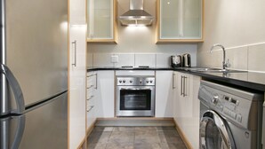 Eine kompakte Küche mit Edelstahl-Kühlschrank, Backofen und Waschmaschine, Holzschränken und einer gefliesten Spritzschutzwand.