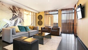 Ein modernes Wohnzimmer mit einer Couch, Sesseln, einem Couchtisch und einem an der Wand befestigten Flachbildfernseher.