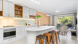 A modern kitchen with white cabinetry, a central island with stools, and a view to an outdoor balcony.