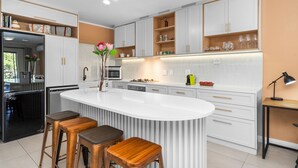 A modern kitchen with white cabinetry, a central island with stools, and a built-in oven.