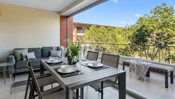 A balcony with a dining table set for two, a sofa, and a bench.