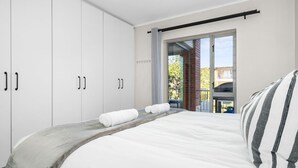 A bedroom with a bed, white wardrobe, and a sliding glass door to a balcony.