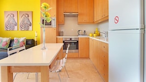 A modern kitchen with wooden cabinets, a white refrigerator, and a dining area with a table and chairs. - Neptune Isle 214 - One Bedroom Apartment, Sleeps 2 (Cape Town)