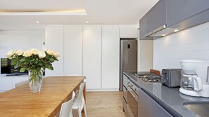Una cocina moderna con armarios blancos, una mesa de comedor de madera y una cafetera.