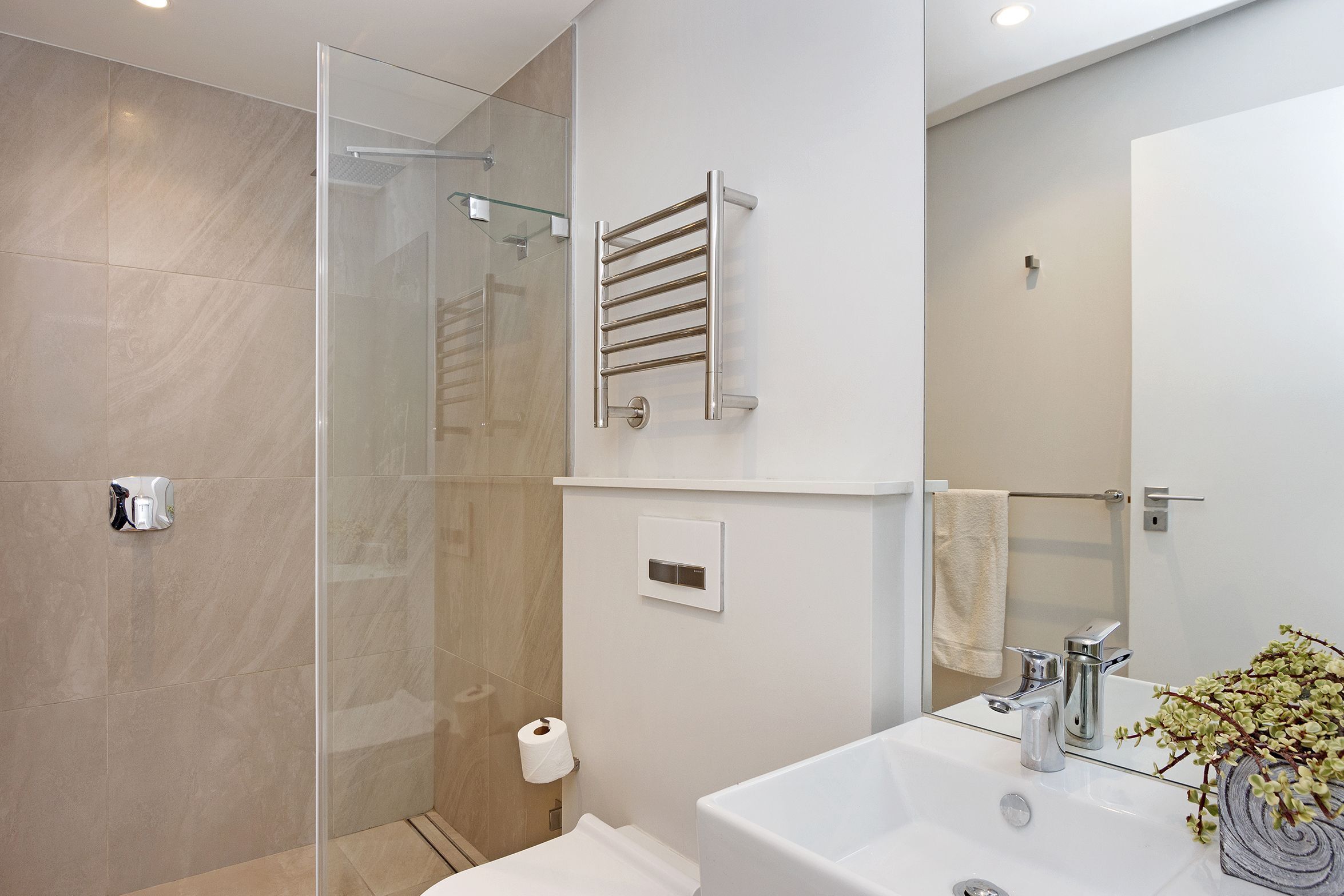 Uma casa de banho moderna com cabine de duche em vidro, lavatório branco com espelho e porta-toalhas.