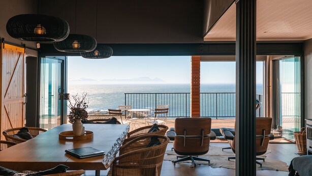 A spacious dining area with a view of the sea, featuring wicker furniture and a wooden table. - Klein-Hangklip - Two Bedroom House, Sleeps 4 (Cape Town)