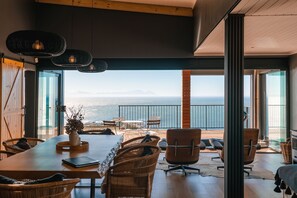 Un vaste espace dédié à la salle à manger, offrant une vue sur la mer, avec des meubles en osier et une table en bois.