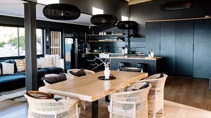 A modern kitchen with a central island, black appliances, and a dining area with wicker chairs and a wooden table. - Klein-Hangklip - Two Bedroom House, Sleeps 4 (Cape Town)