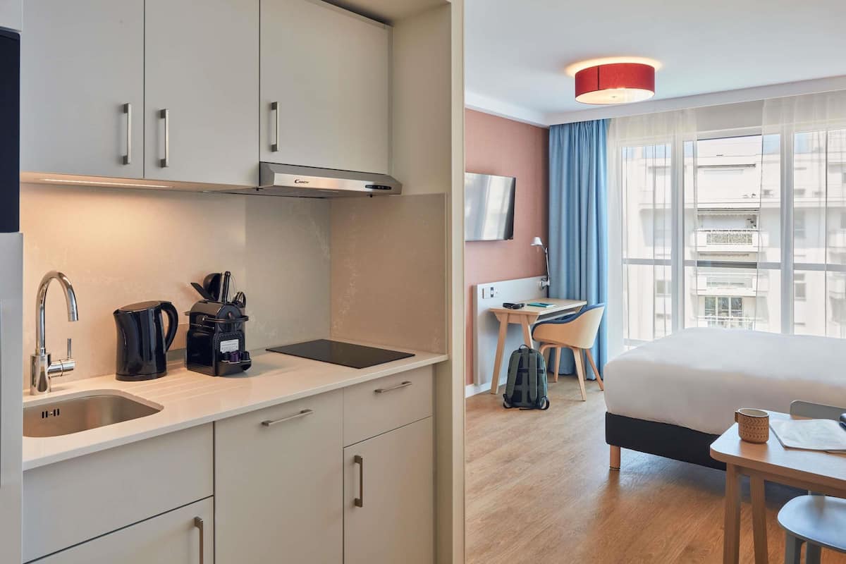 Une chambre d’hôtel moderne équipée d’une kitchenette, d’un lit, d’un bureau et d’une télévision.