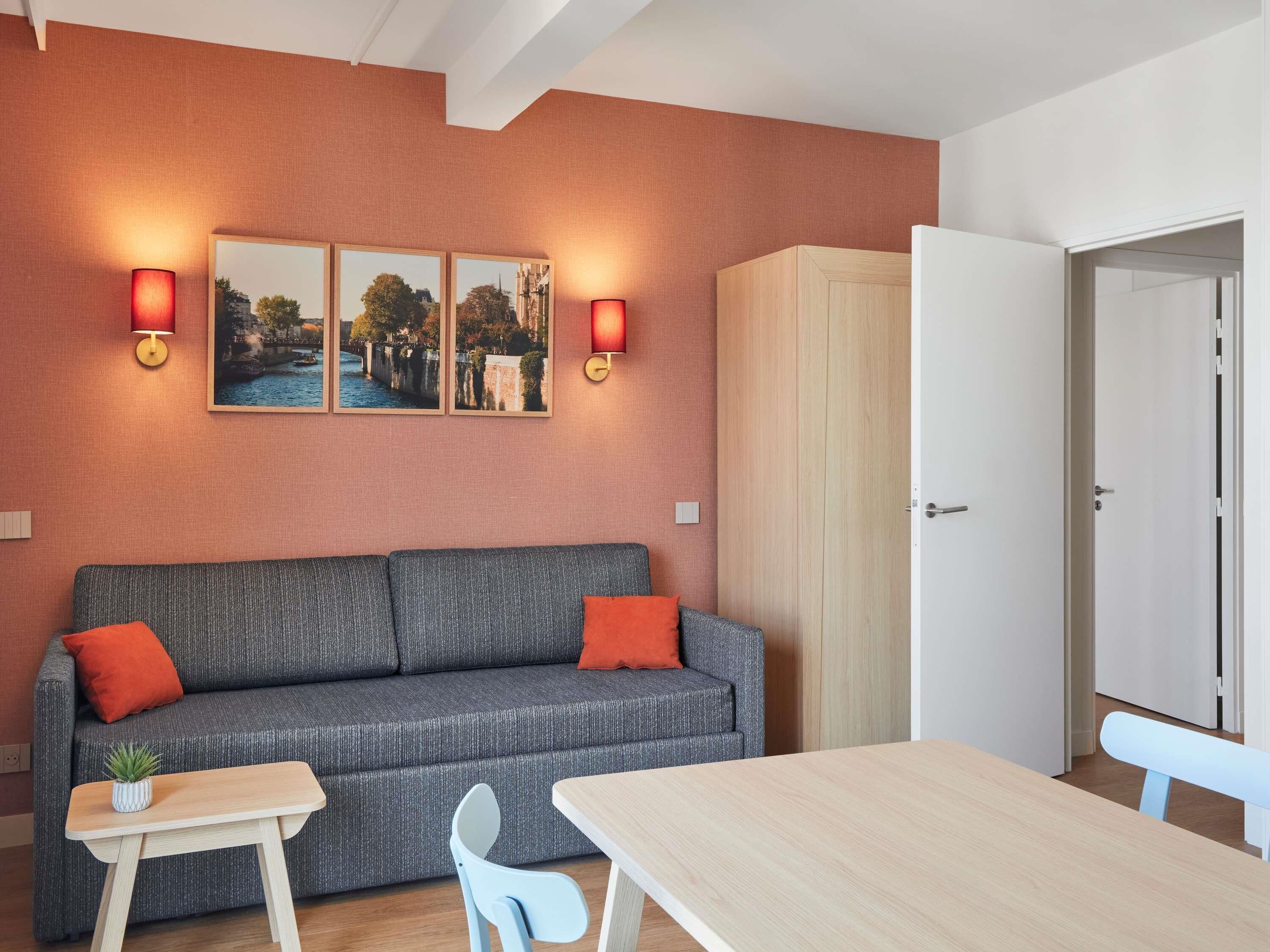 A modern room with a grey sofa, two red wall sconces, a wooden cabinet, and a white door.