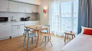 Ein modernes Hotelzimmer mit Küchenzeile, Essbereich und großem Fenster mit Vorhängen.
