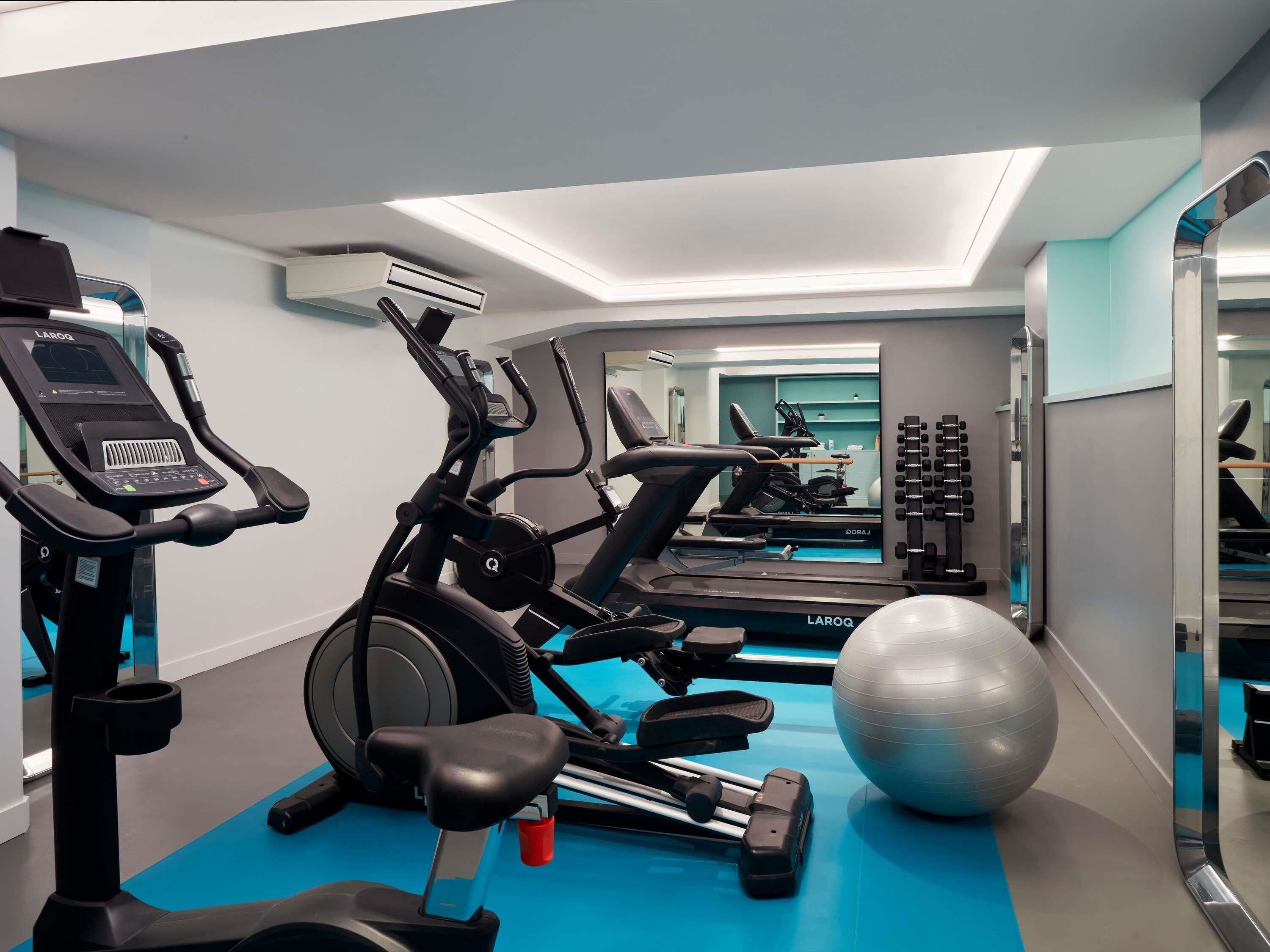 A gym with exercise equipment, a mirrored wall, and a blue floor.