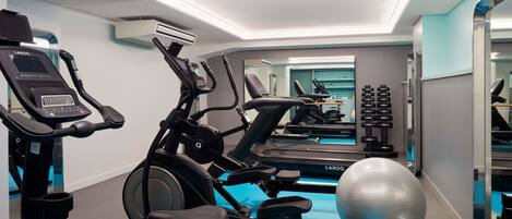 A gym with exercise equipment, a mirrored wall, and a blue floor.