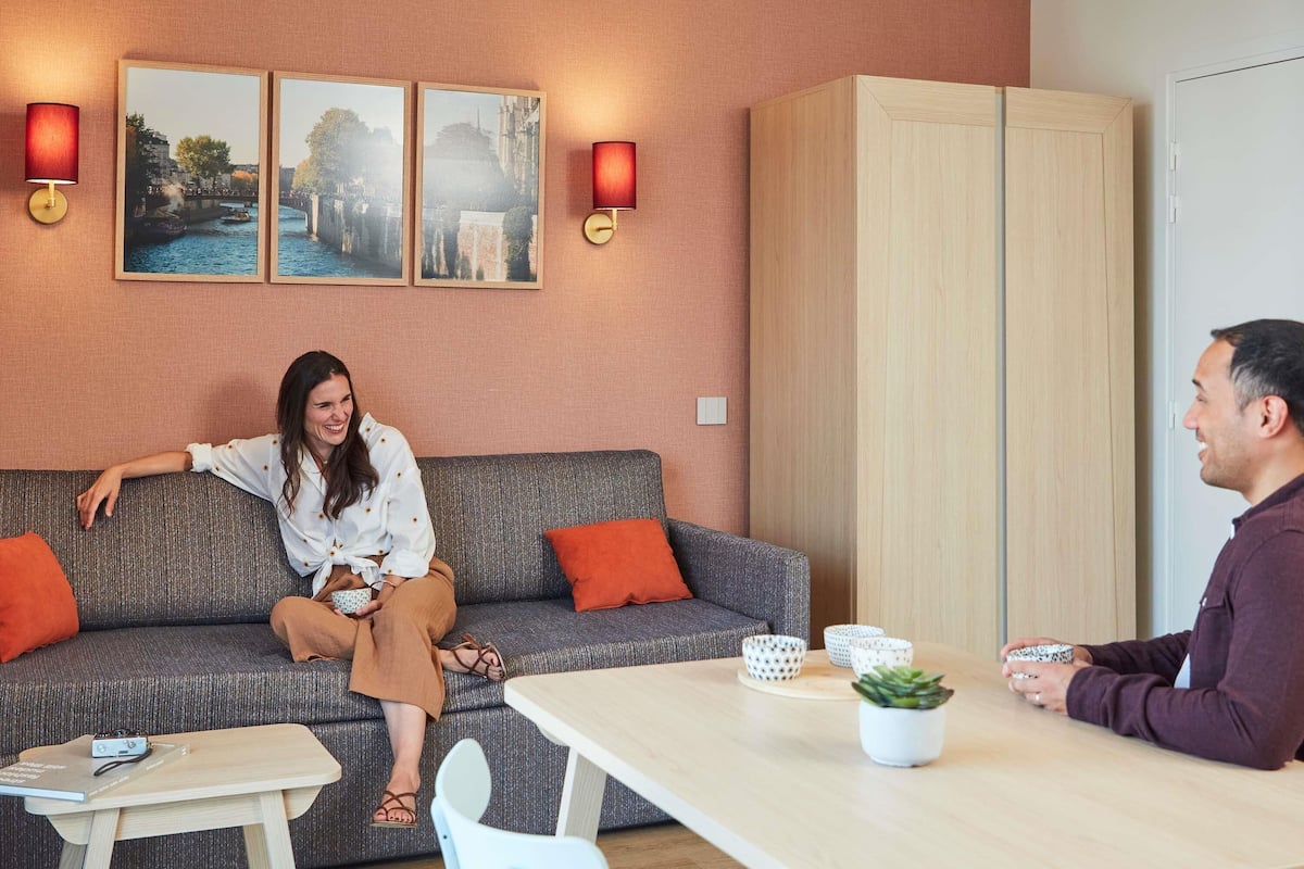 Un salon moderne avec un canapé, une table et un meuble. Deux lampes sont fixées au mur et trois tableaux encadrés y sont accrochés.
