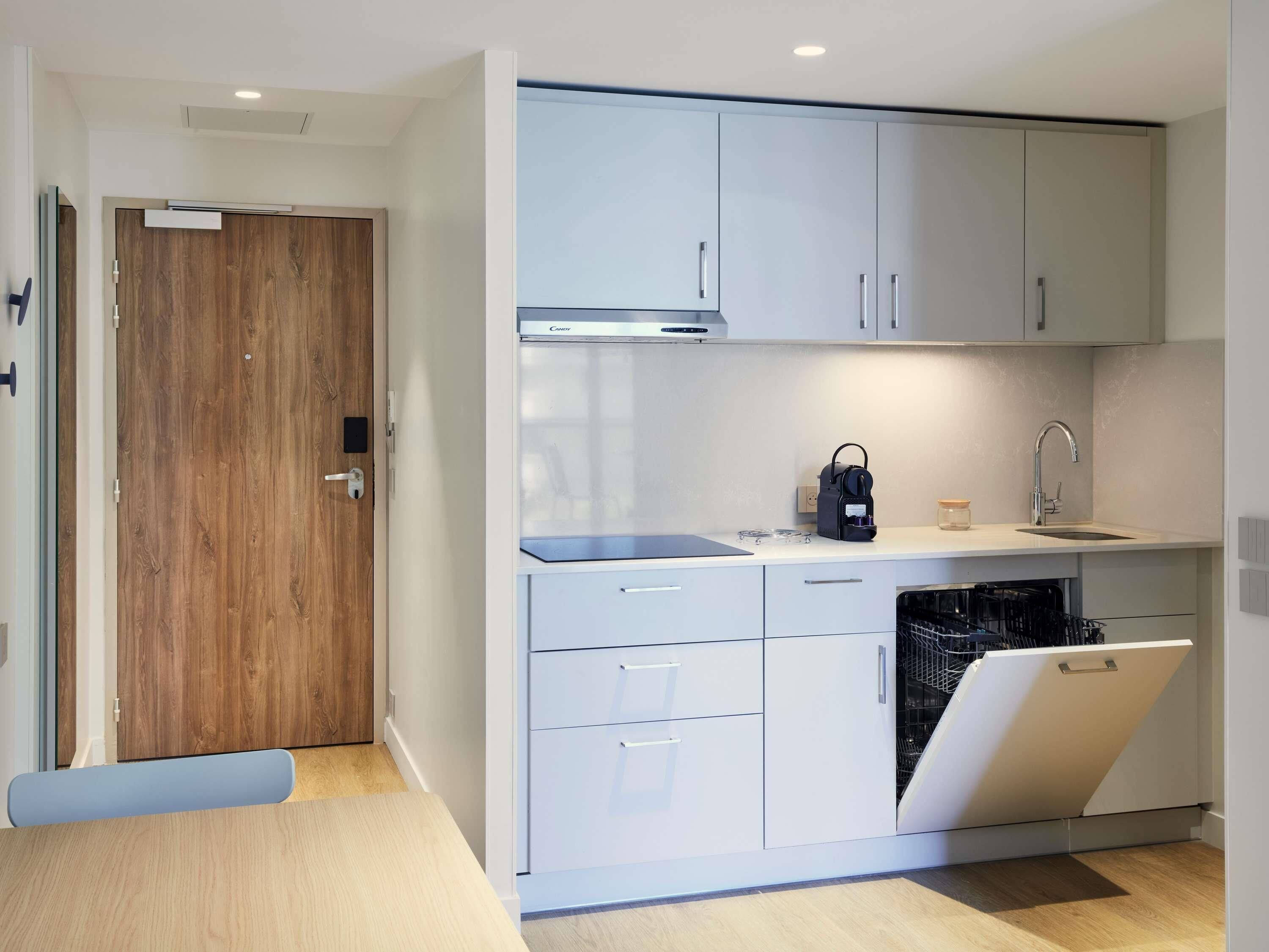 A modern kitchen with white cabinets, a built-in dishwasher, and a coffee machine.