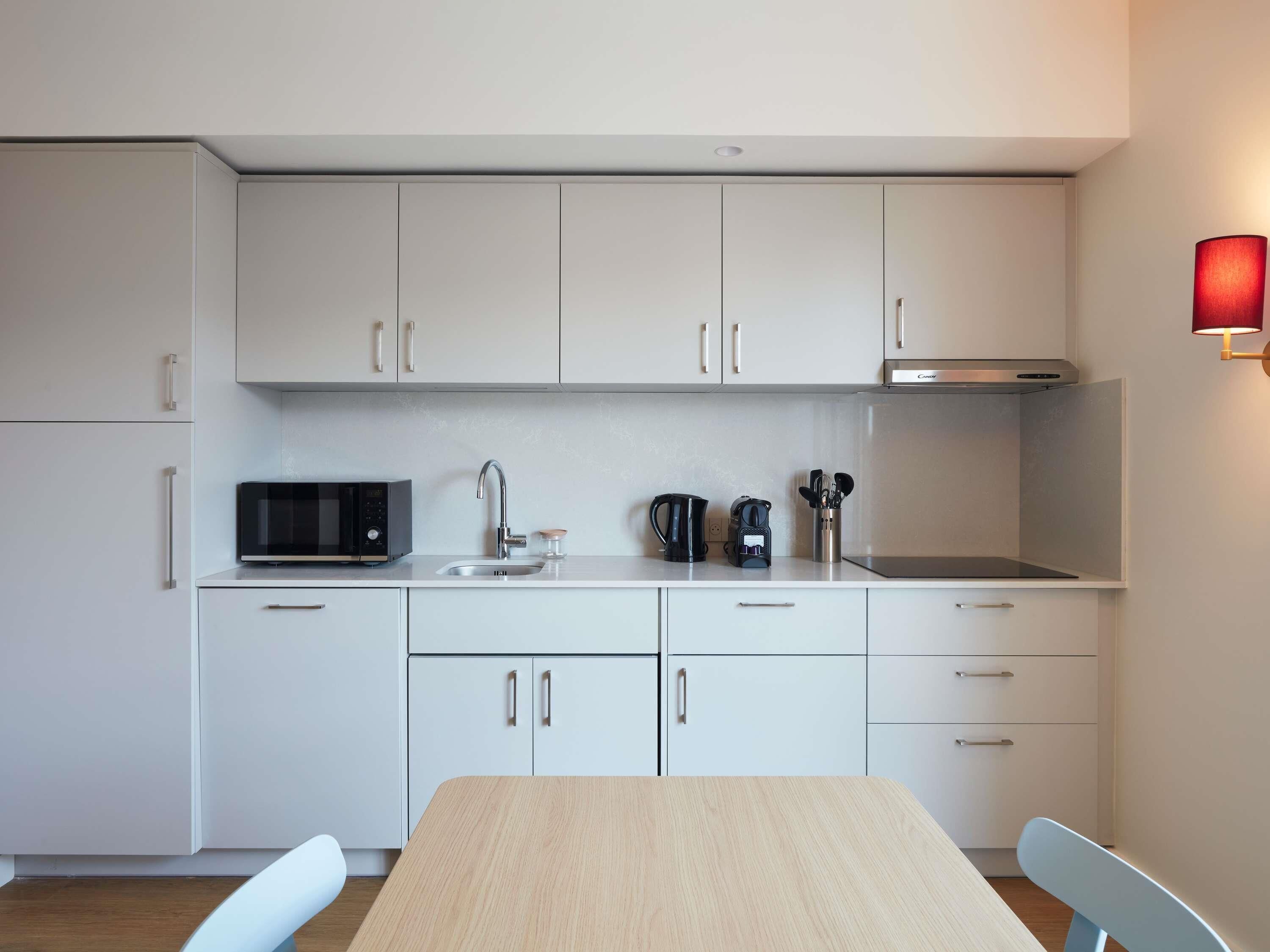 A modern kitchen with white cabinets, a microwave, a coffee maker, and a kettle.