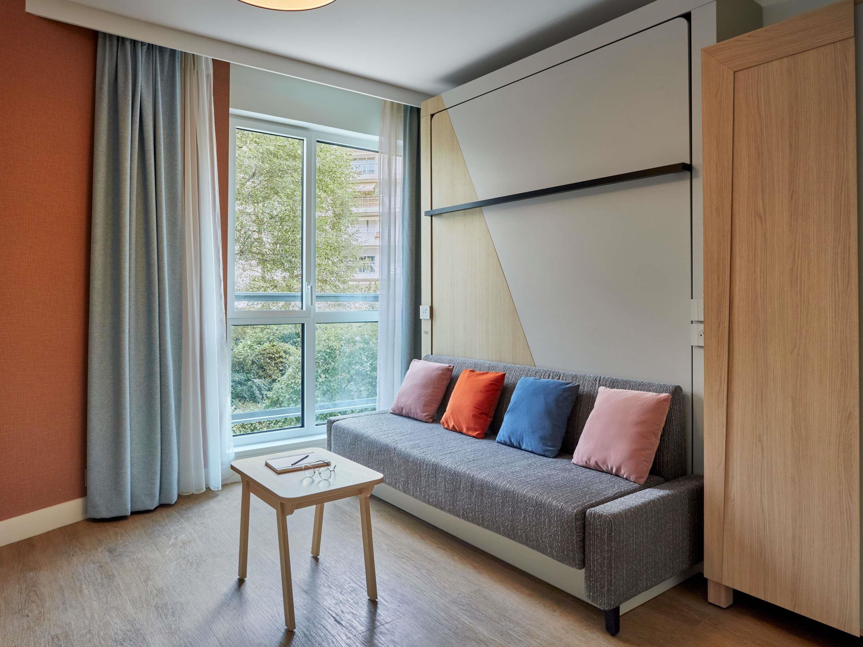 Ein Zimmer mit einer Couch, einem kleinen Tisch, einem Kleiderschrank und einem Fenster mit Vorhängen.