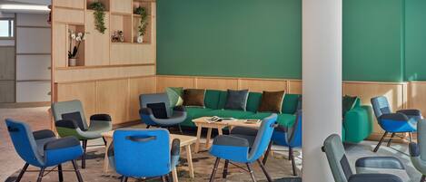 A modern lounge area with a green wall, wooden shelving, and blue and grey upholstered chairs.