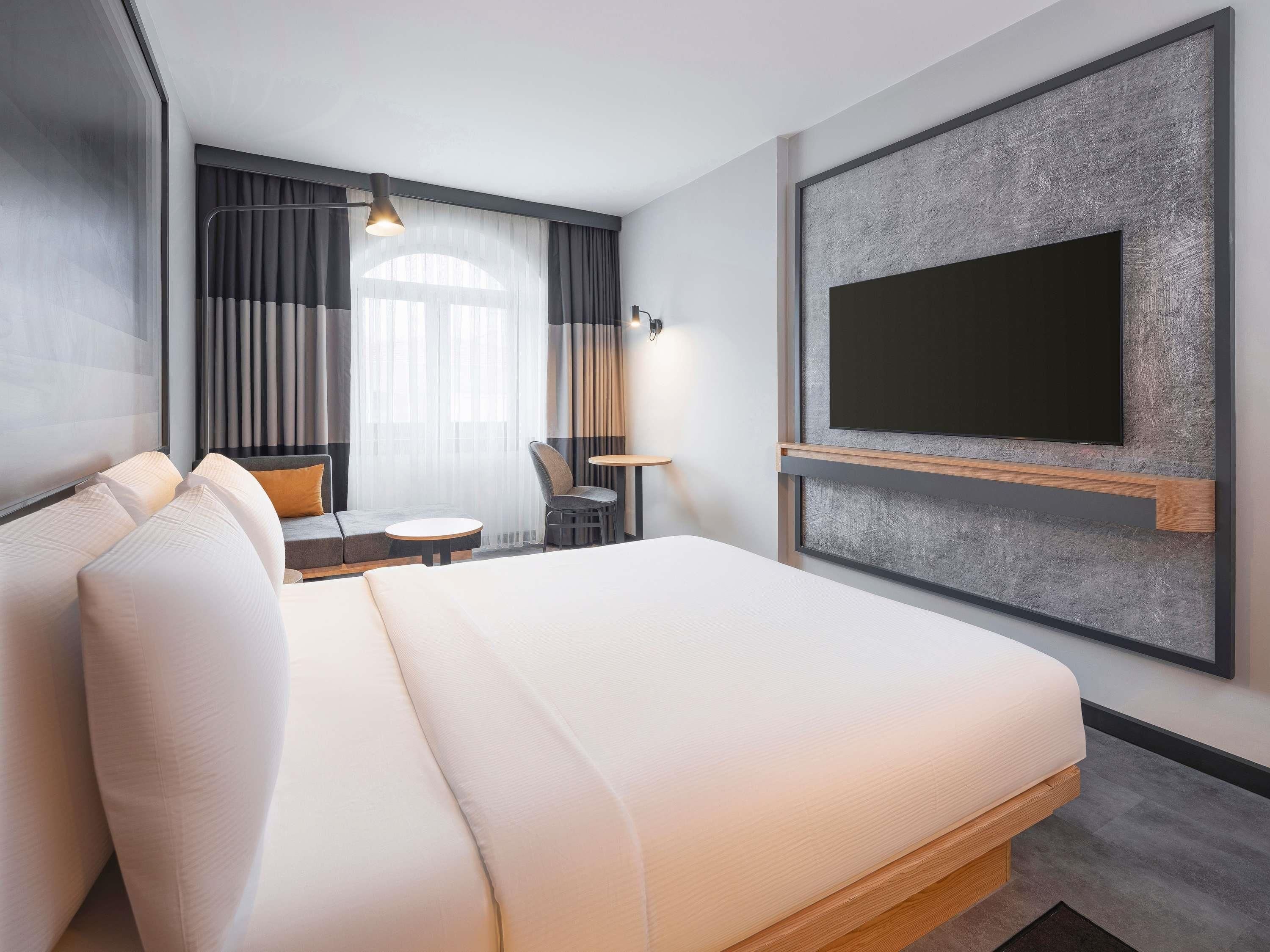 Moderni hotellihuone, jossa on suuri sänky, työpöytä, tuoli ja seinälle asennettu televisio.