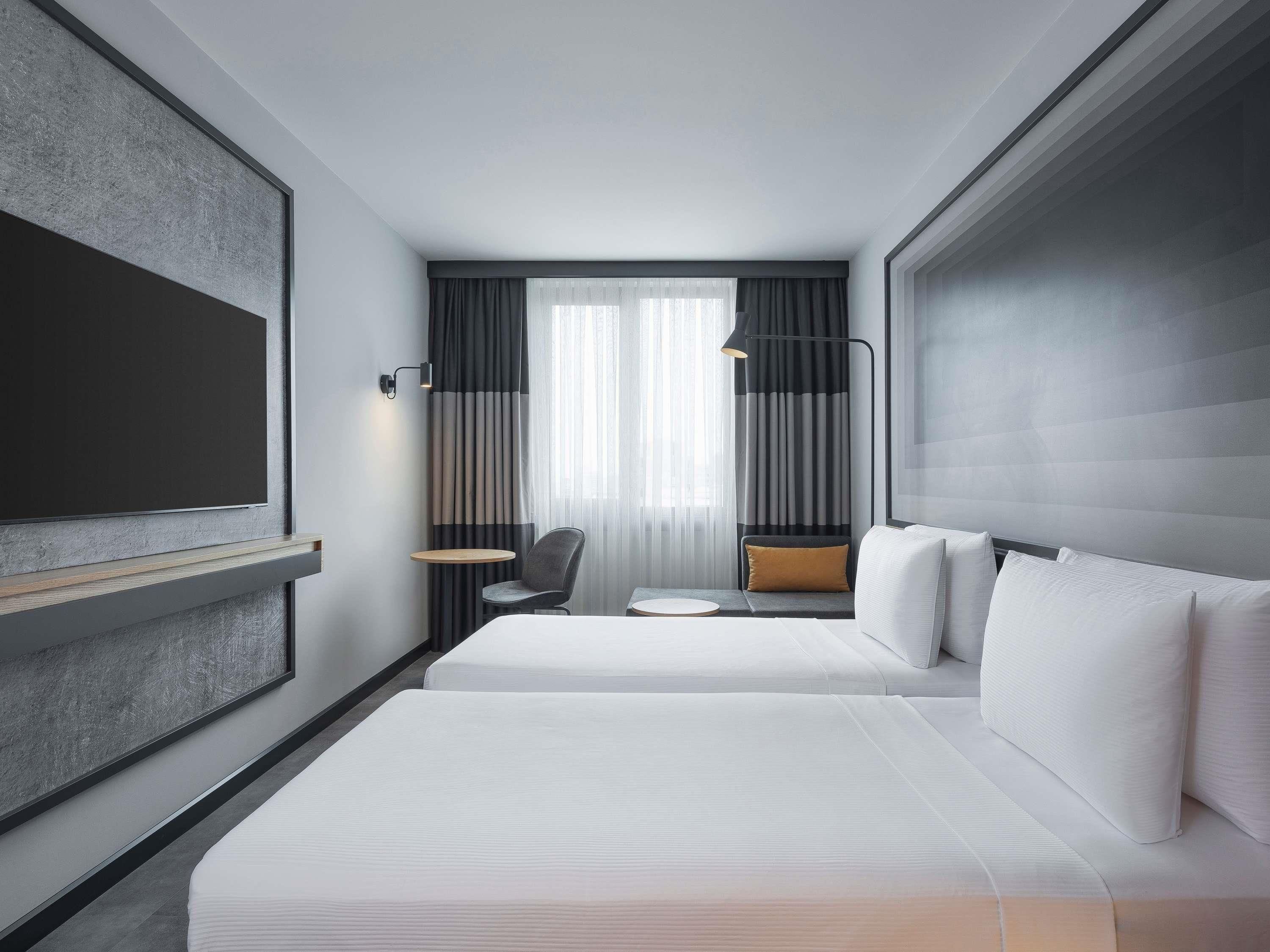 A modern hotel room with two beds, a TV, a small table, and a chair.