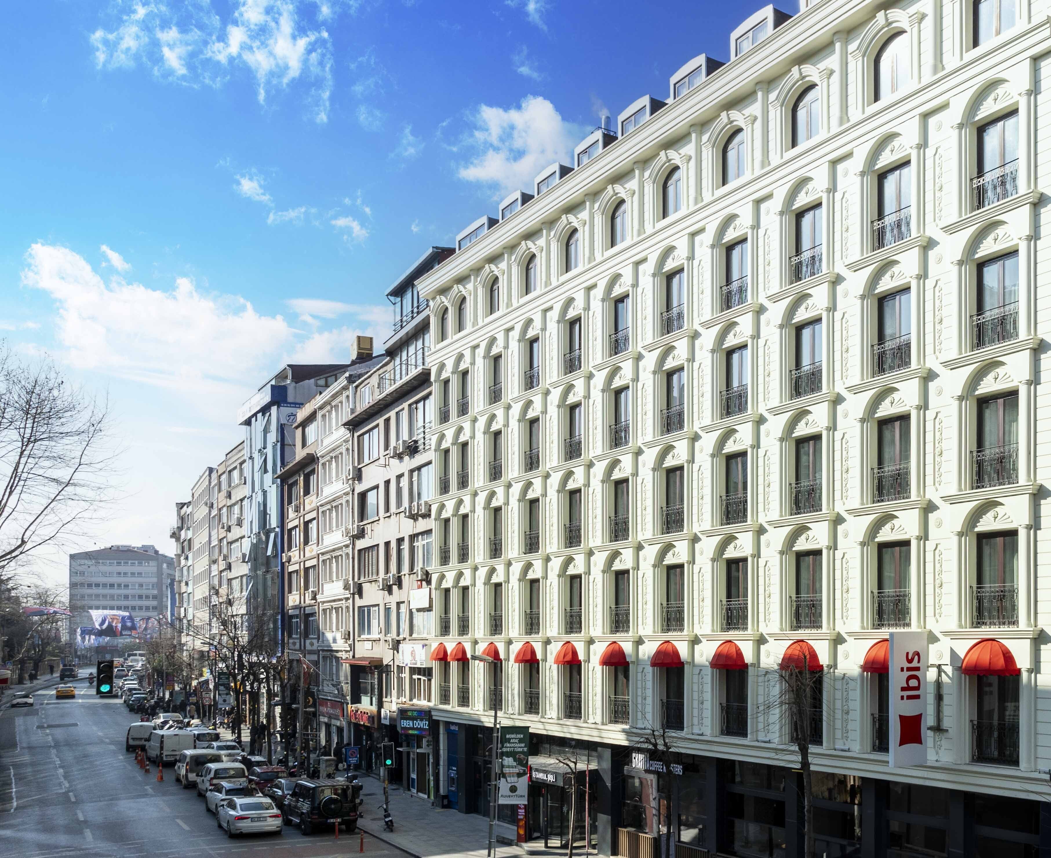 A multi-story building with a row of shops on the ground floor, including a visible 'ibis' sign.