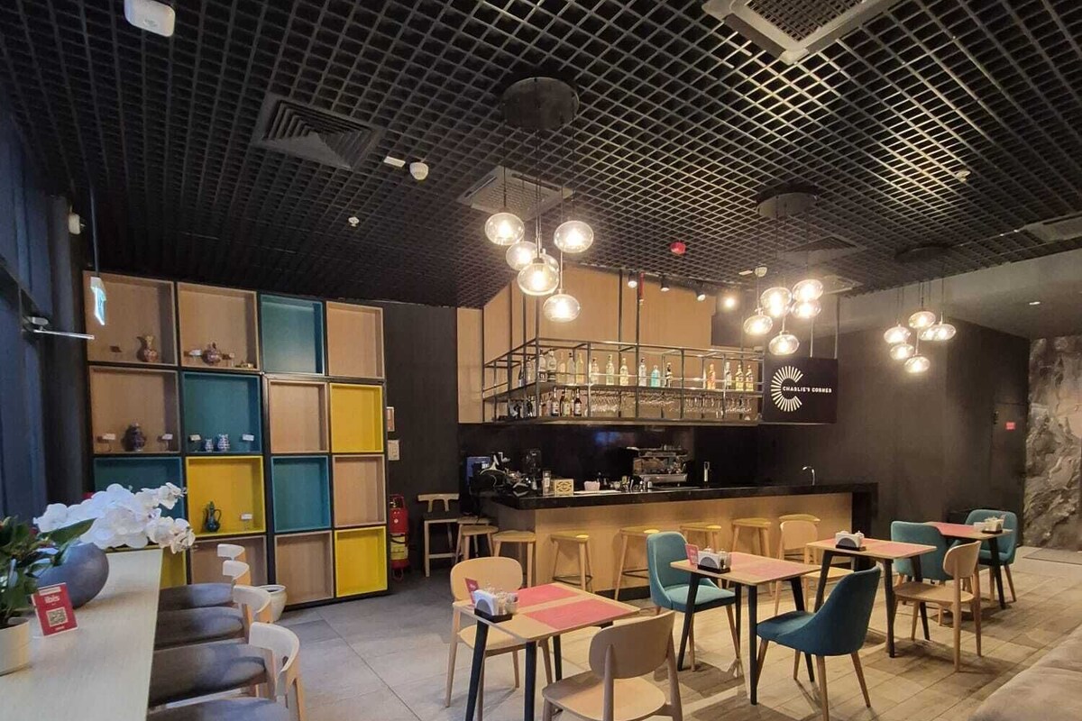 A modern cafe with a grid-patterned ceiling, a bar area, and various seating options including tables and chairs.