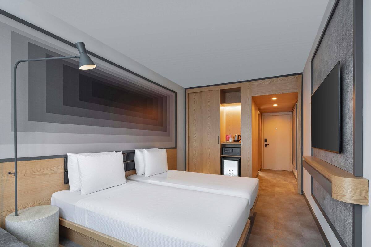 A modern hotel room with a large bed, a desk, a flat-screen TV, and a walk-in closet.