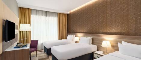 A hotel room with two beds, a desk with a TV, a chair, and a window with curtains.