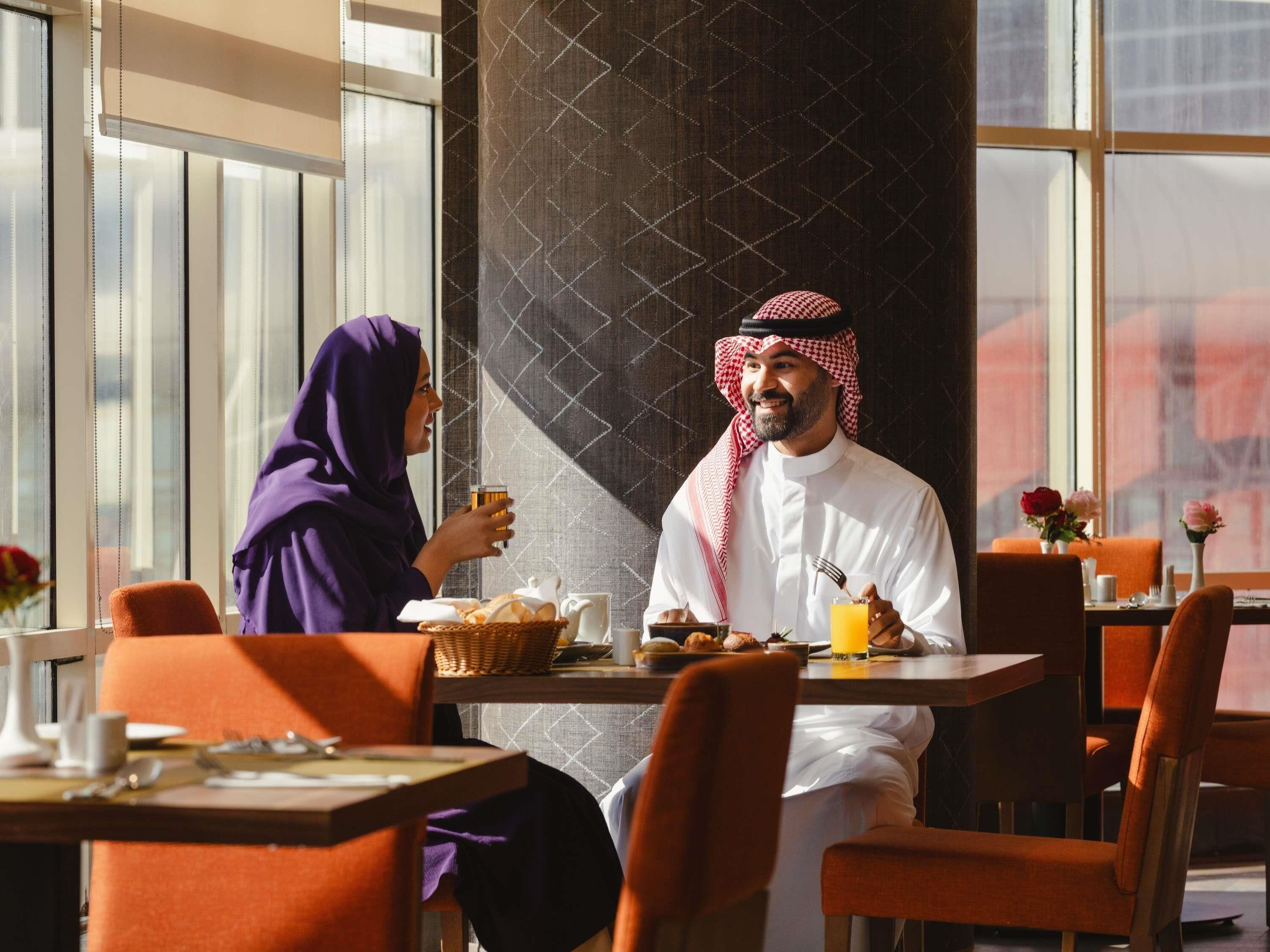 Ein Mann und eine Frau sitzen an einem Tisch in einem Café mit Blick auf die Stadt durch große Fenster.