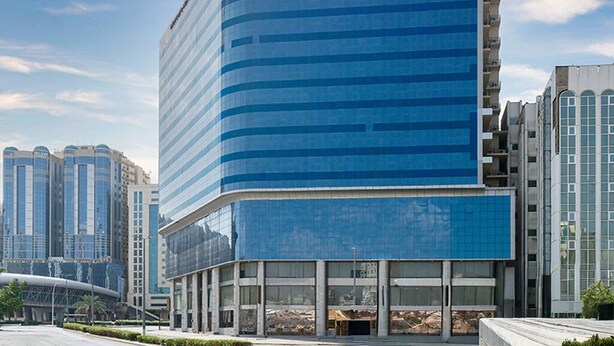A modern, curved building with a glass facade, surrounded by other high-rise buildings. - Mercure Makkah Aziziah (Makkah)