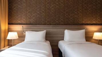 Quarto de hotel com duas camas, cabeceira de madeira, papel de parede estampado e luminárias de cabeceira.
