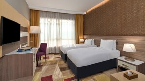 A hotel room with two beds, a desk with a flat-screen TV, a chair, and a nightstand with a lamp. - Mercure Makkah Aziziah (Makkah)