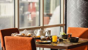 Une table de petit-déjeuner avec des chaises orange, une table en bois et une vue sur la fenêtre.