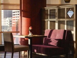 Een kamer met een bank, een stoel, een tafel met een vaas en een raam met uitzicht op gebouwen.