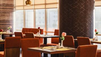 A restaurant interior with tables and chairs, large windows, and decorative vases with flowers.