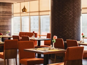 A restaurant interior with tables and chairs, large windows, and decorative vases with flowers. - Mercure Makkah Aziziah (Makkah)