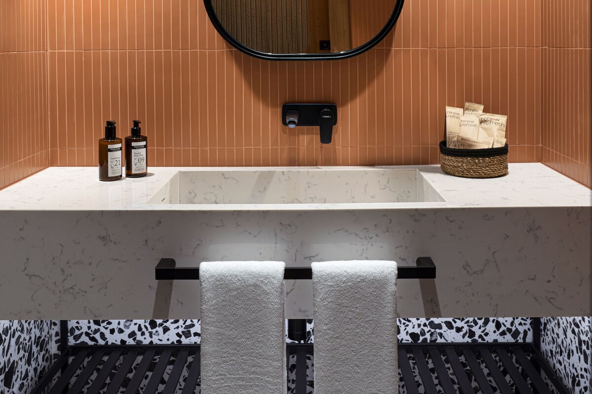 Un baño moderno con un espejo grande, dos botellas de champú y un perchero para toallas.