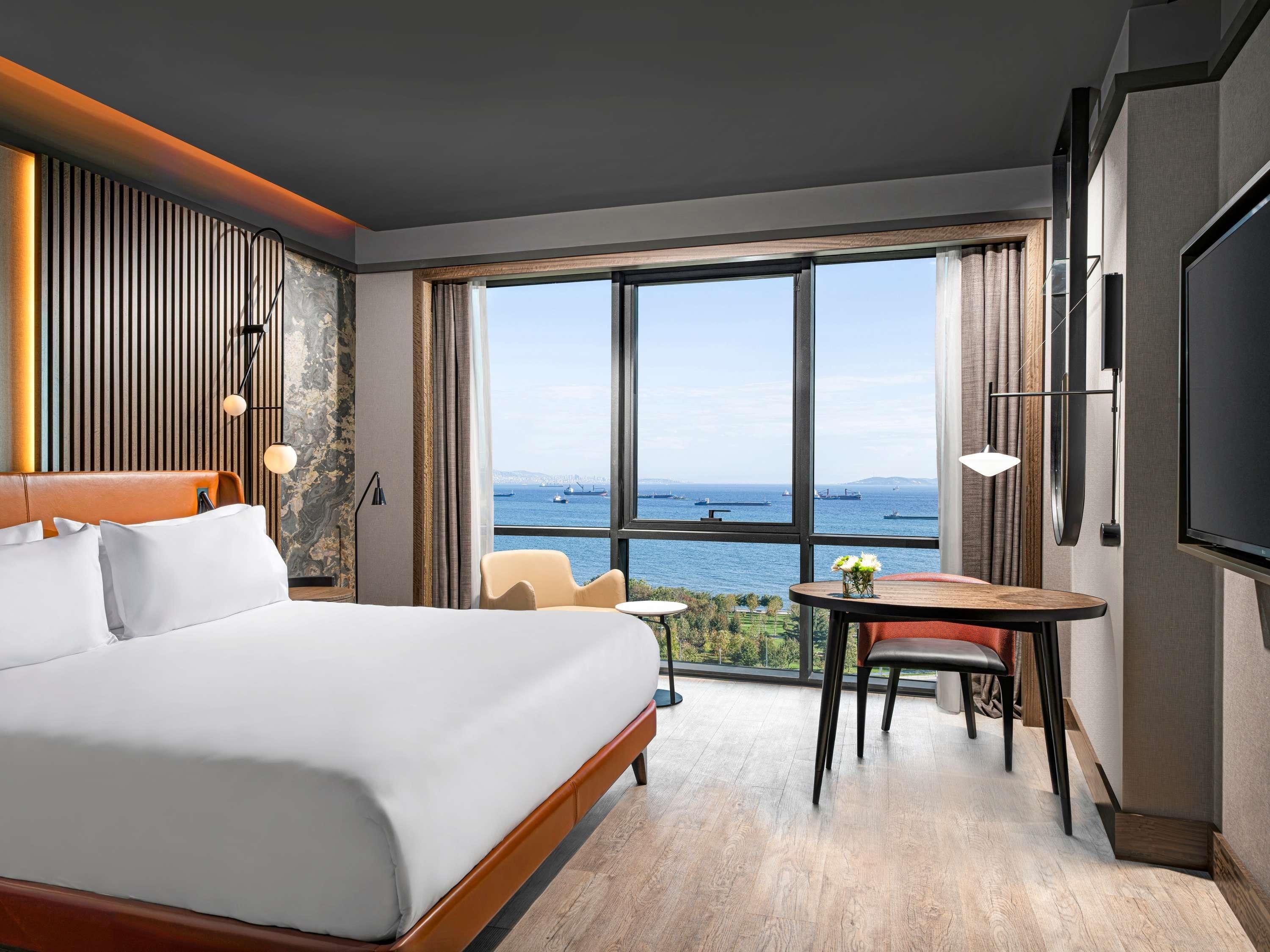 Quarto de hotel com uma cama grande, área de jantar e vista para o mar.