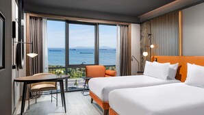 Une chambre d’hôtel avec deux lits, une petite table, une chaise et une vue sur la mer.