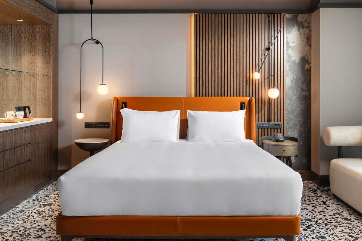 A modern hotel room with a large bed, bedside tables, a built-in wardrobe, and a unique textured wall.
