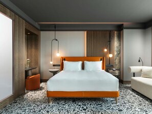 Ein modernes Hotelzimmer mit einem großen Bett, einem kleinen Beistelltisch, einem Nachttisch, einem Sofa und einer Wandlampe.