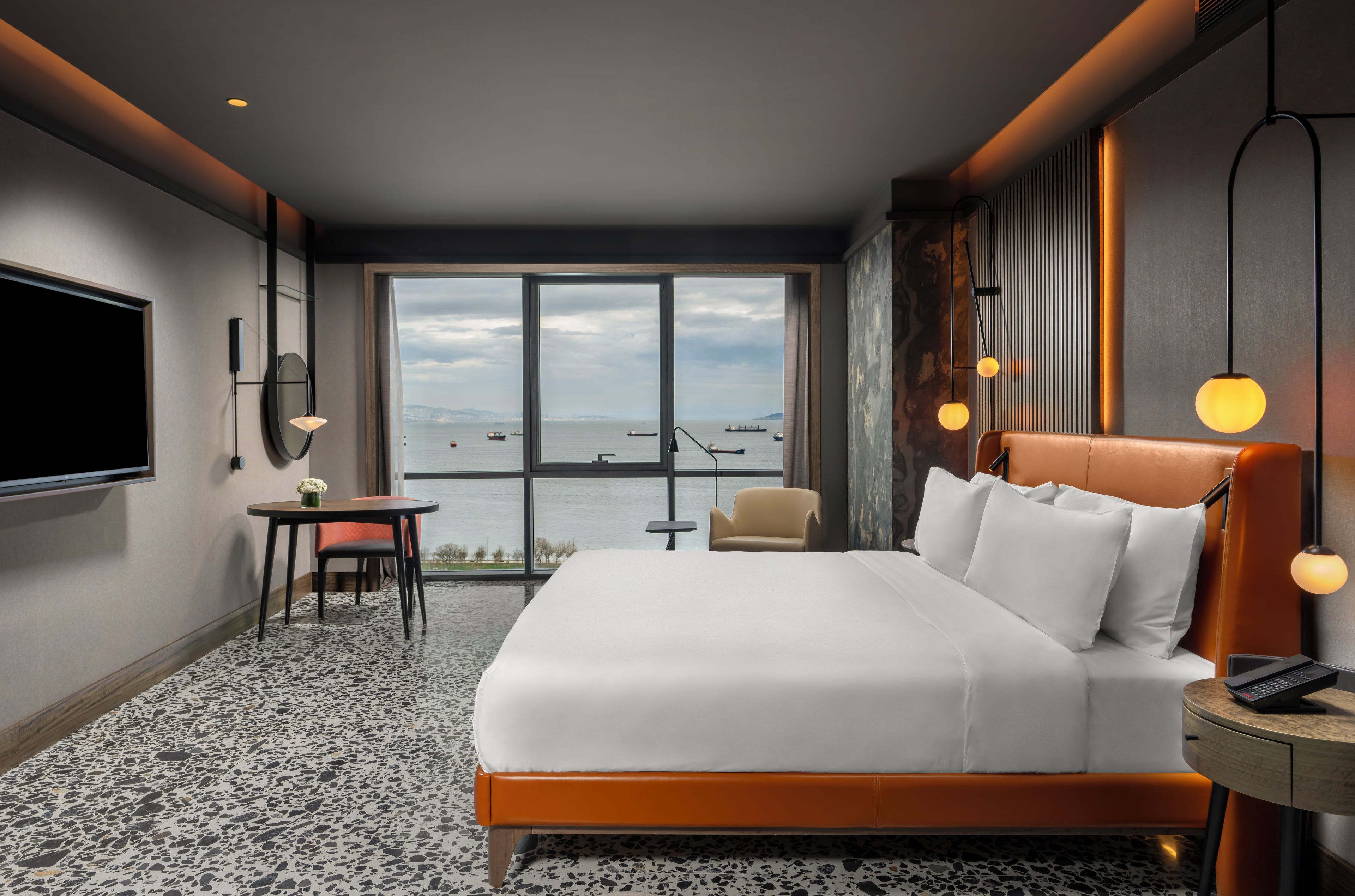 Habitación de hotel con una cama grande, un escritorio, una silla, un televisor y vista al mar.