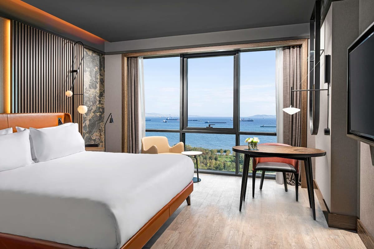 A hotel room with a large bed, a dining area, and a view of the sea.