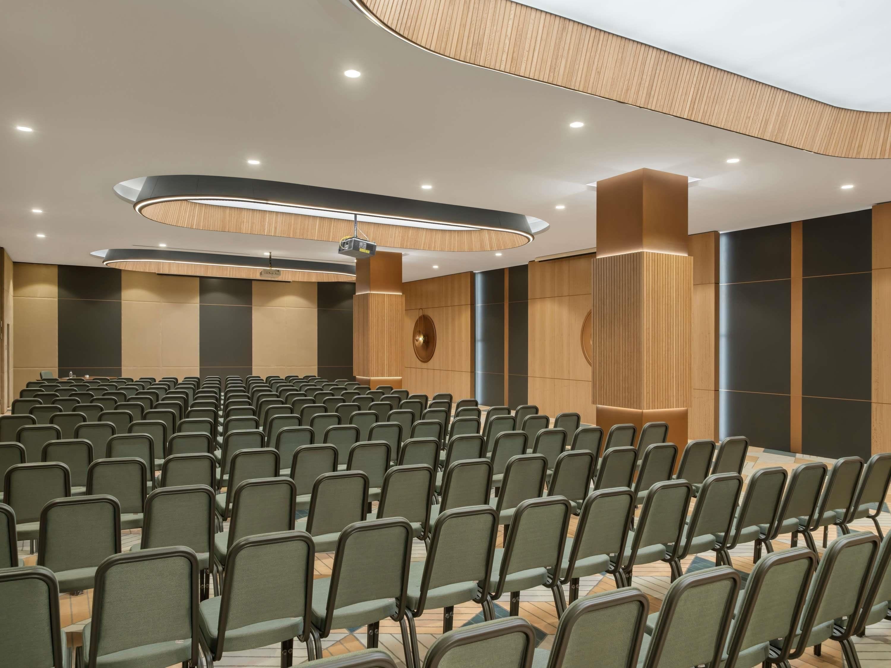 A conference room with rows of chairs, a podium, and a large screen.
