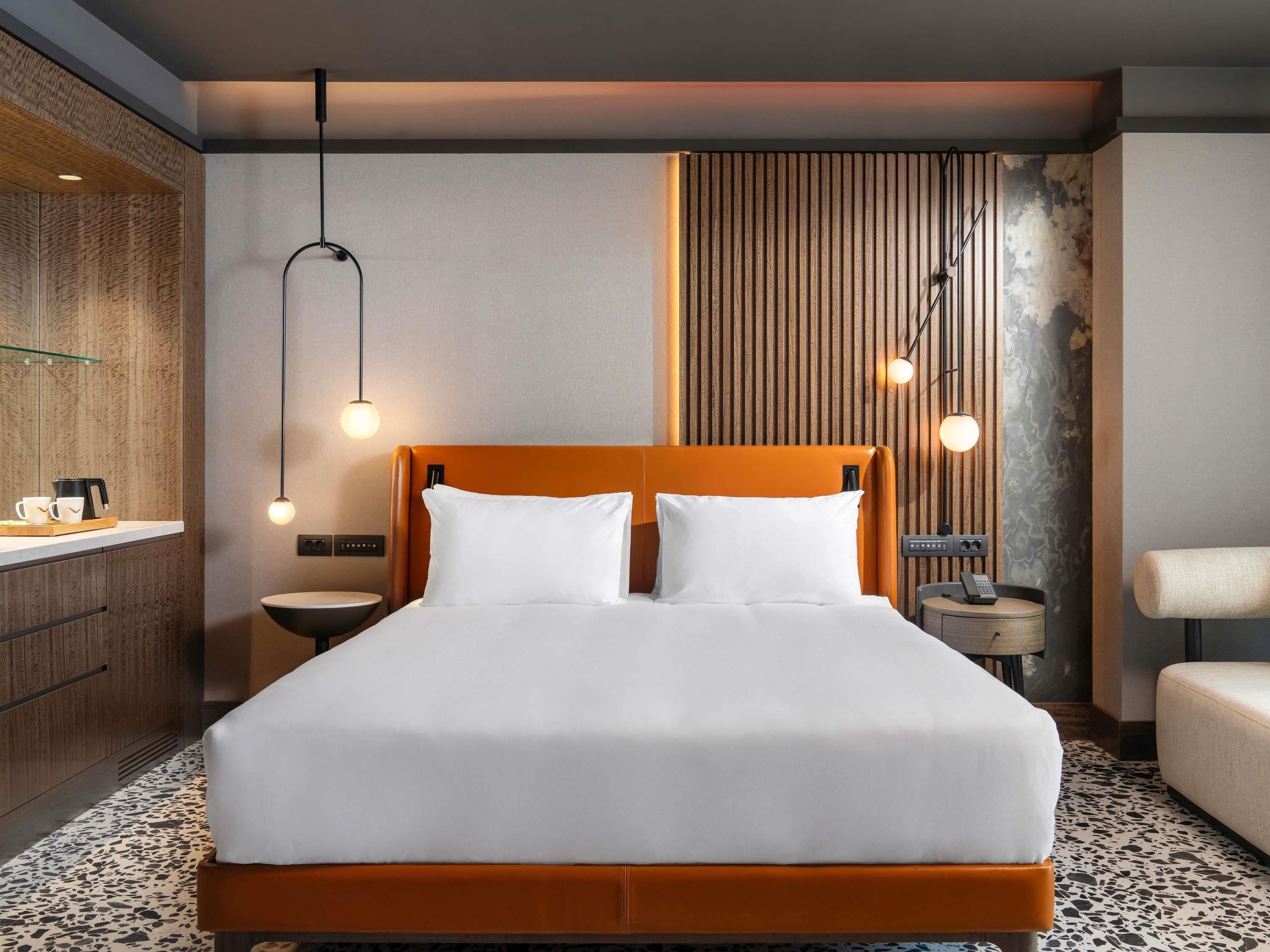 Una habitación de hotel moderna con una cama grande, mesitas de noche, un armario empotrado y una pared con una textura única.